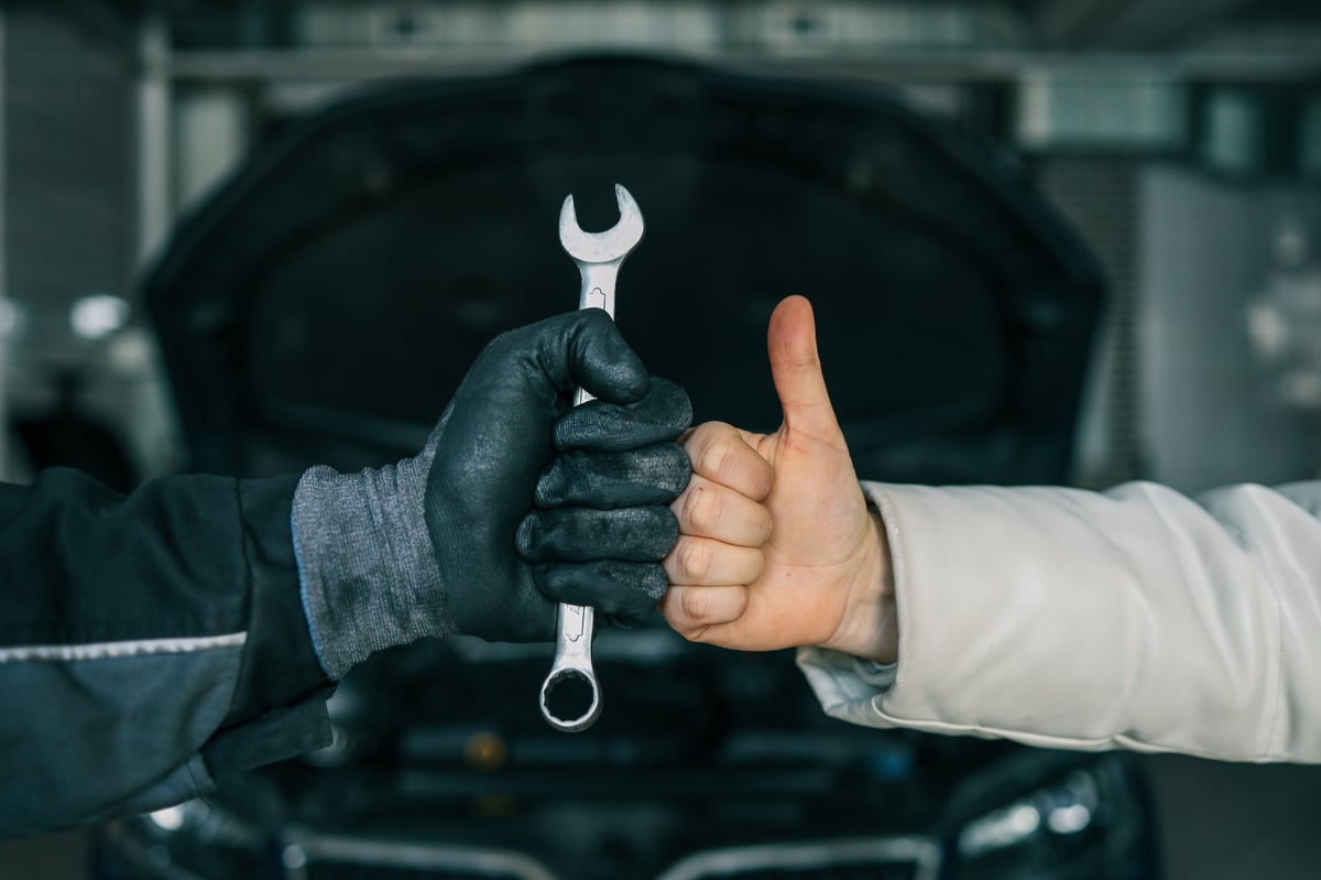 Mechanic's gloved hand holding a wrench next to a satisfied customer's hand giving a thumbs-up