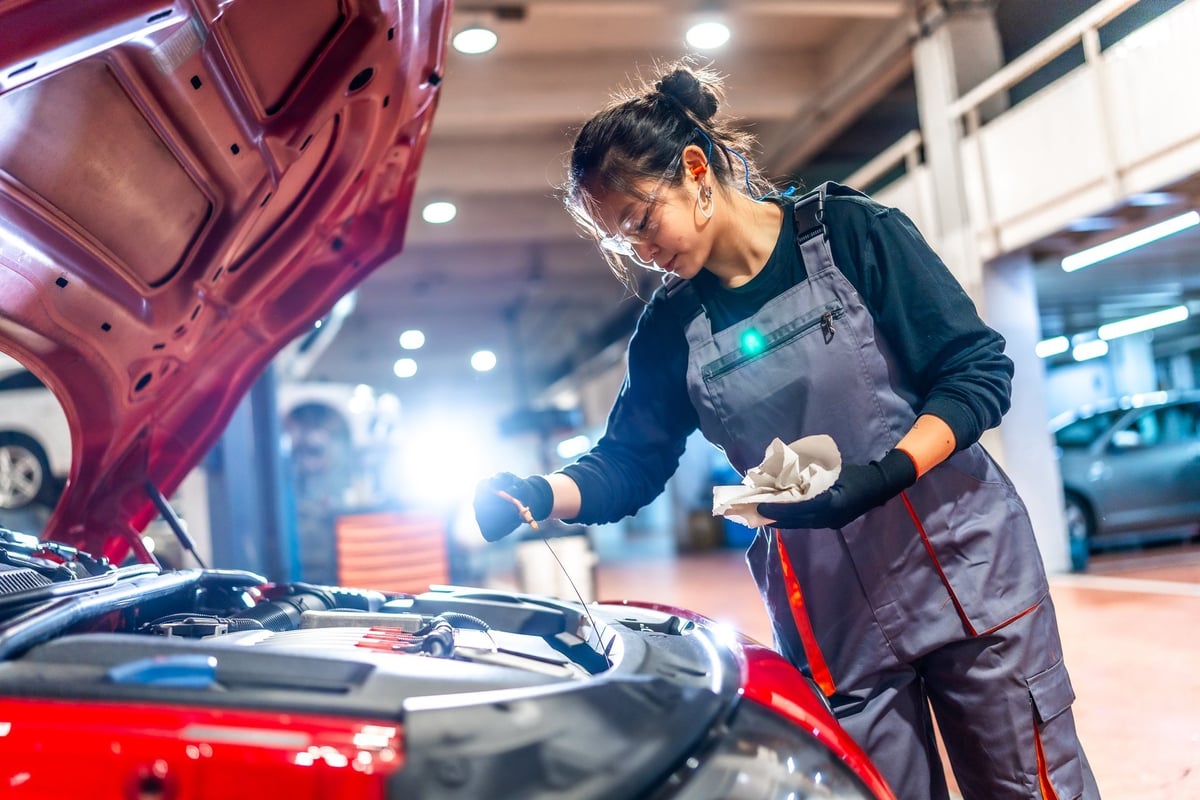 Mechanic in overalls and protective glasses checking the oil level of a car engine in a garage