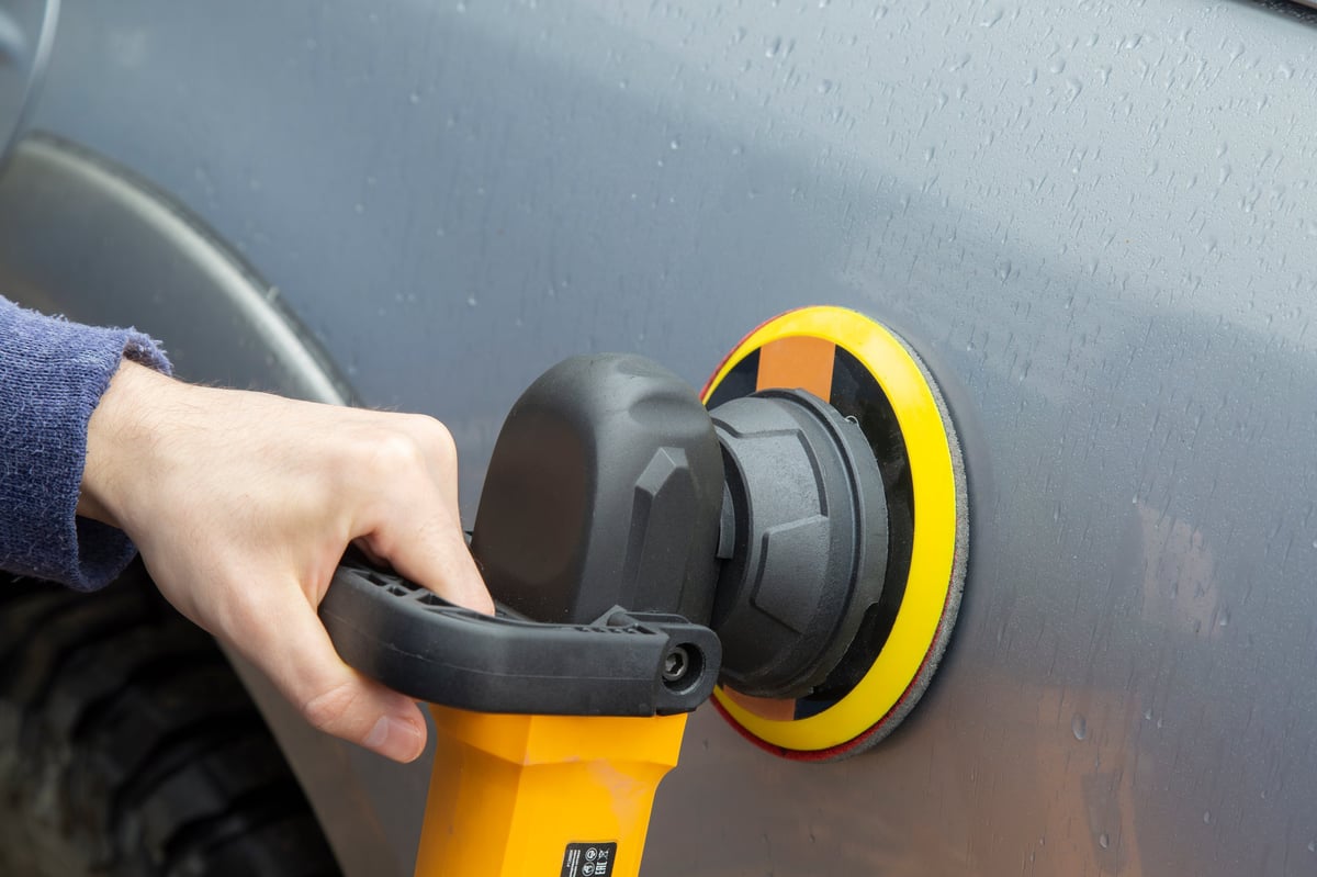 Technician polishing a repaired car body with a grinder after bodywork