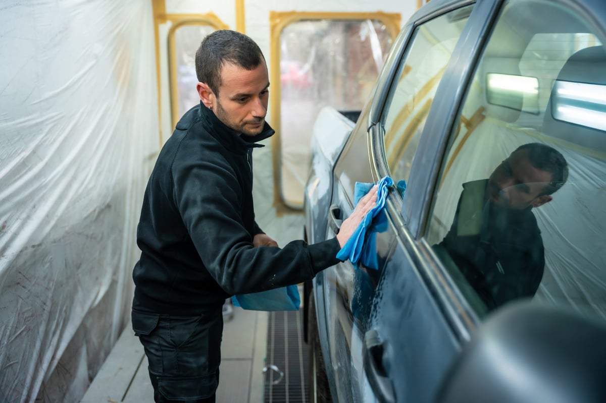 Auto body technician cleaning and prepping a car in a paint booth before painting