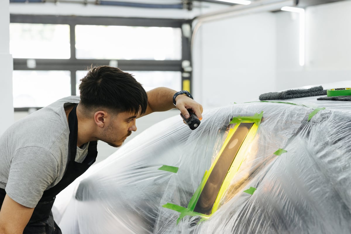 Focused mechanic polishing a masked car panel inside a bright workshop during body repair